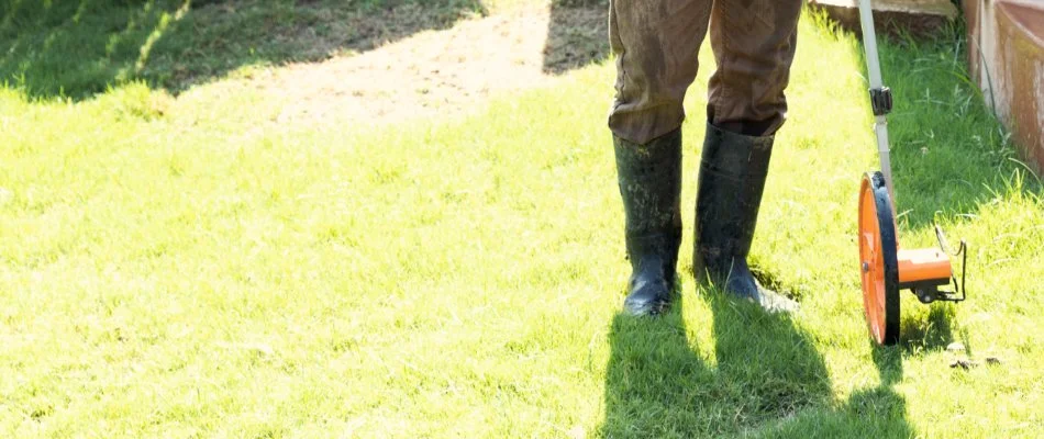 A professional in Plano, TX, using a measuring wheel to measure an irrigation system zone on a lawn. 